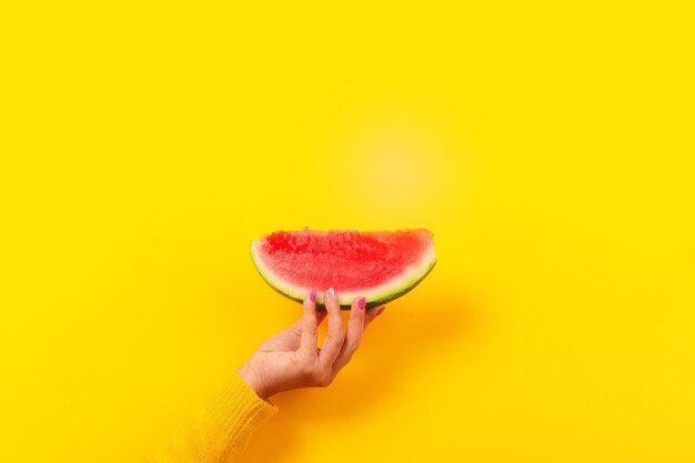 Mão segurando uma fatia de melancia sobre o amarelo