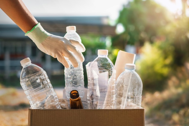 Foto mão segurando uma garrafa de plástico de lixo colocando em um saco de reciclagem para limpeza