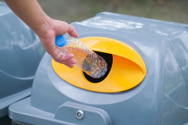 Mão segurando uma garrafa de plástico e jogando no lixo para reciclagem.