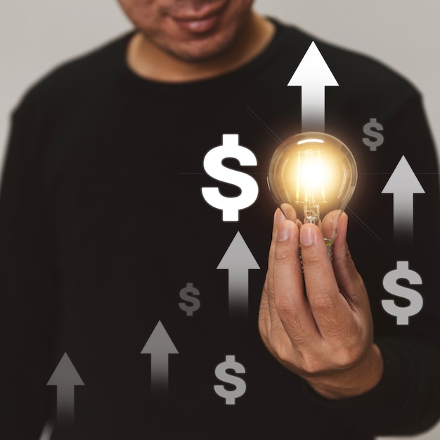 Foto mão segurando uma lâmpada se levanta com uma seta de investimento para o crescimento dos negócios