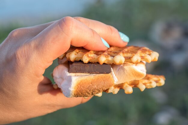 Mão segurando uma mancha quente. sobremesa doce feita de biscoitos, chocolate e marshmallow