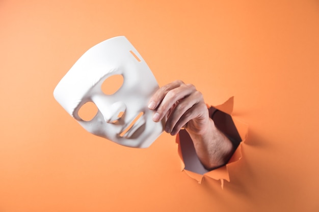 Mão segurando uma máscara branca em fundo laranja