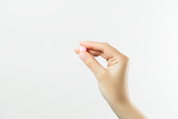 Foto mão segurando uma pílula rosa redonda em um fundo branco