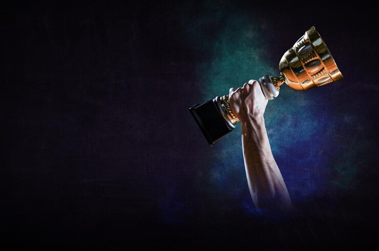 Foto mão segurando uma taça de troféu de ouro contra um fundo escuro. mídia mista
