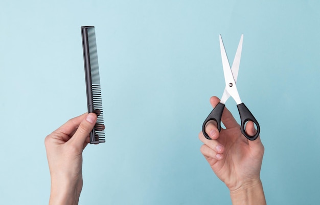 Mão segurando uma tesoura e escova de cabelo em fundo azul Conjunto para cortes de cabelo barbearia