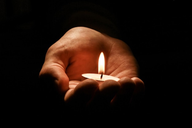 Mão segurando uma vela em um fundo preto