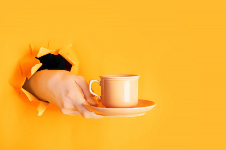 Foto mão segurando uma xícara de café através de um buraco na parede de papel açafrão rasgado ou laranja claro