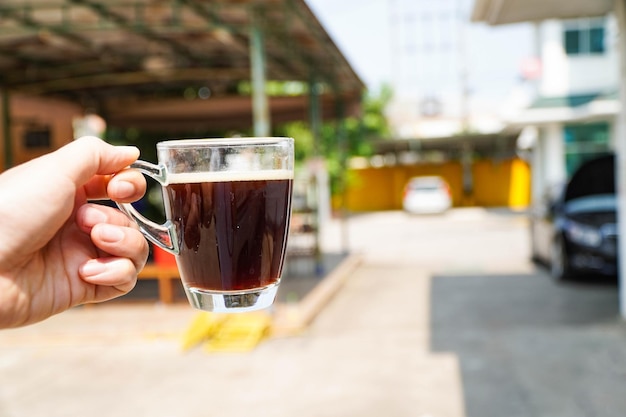 Mão segurando uma xícara de café transparente na mão em um dia quente de café preto em copo de vidro