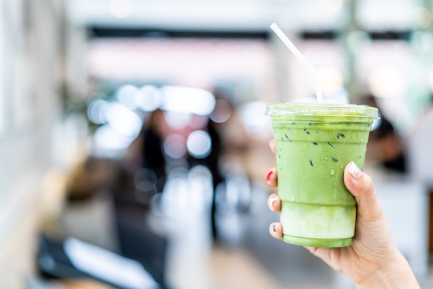 Mão segurando uma xícara de chá verde matcha com leite gelado