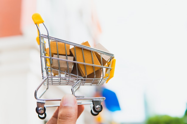 Mão segure a caixa de papel no carrinho de compras mini usando como e-commerce, compras on-line e conceito de marketing de negócios