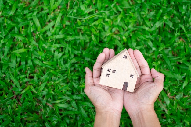 Mão segure modelo de casa em fundo de grama verde e investimento empresarial para conceito imobiliário