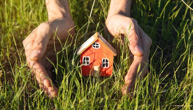 Mão segure o modelo de casa no fundo da grama verde Conceito de casa ecológica