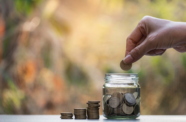 Mão soltar uma moeda com pilha de moedas de dinheiro crescendo para os negócios.