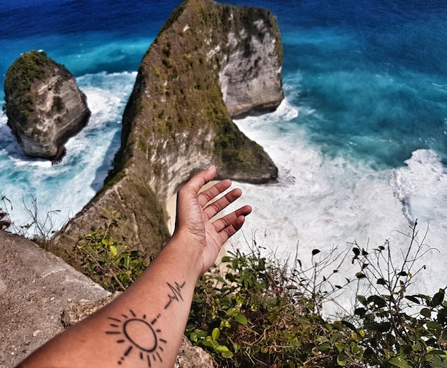 Foto mão tatuada cortada de pessoa gestando em direção ao mar