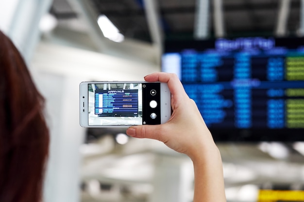 Mão tira foto em smartphone no aeroporto. na tela, o horário de partida do voo