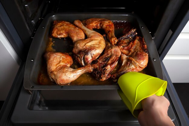 Mão tirando frango do forno na cozinha conceito de comida caseira