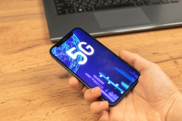 Mão usa telefone celular com rede 5G. Plano de fundo da área de trabalho de negócios. Foto do conceito de internet de alta velocidade, nova geração de redes, dados e conexão, holograma em close-up da tela