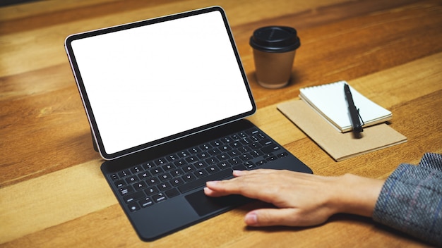 mão usando e tocando o teclado do tablet com tela de desktop branca em branco como computador pc, xícara de café na mesa de madeira