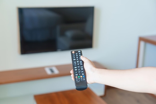 Mão usando o controle remoto para ajustar a Smart TV dentro do quarto moderno em casa Conceito de vida do apartamento