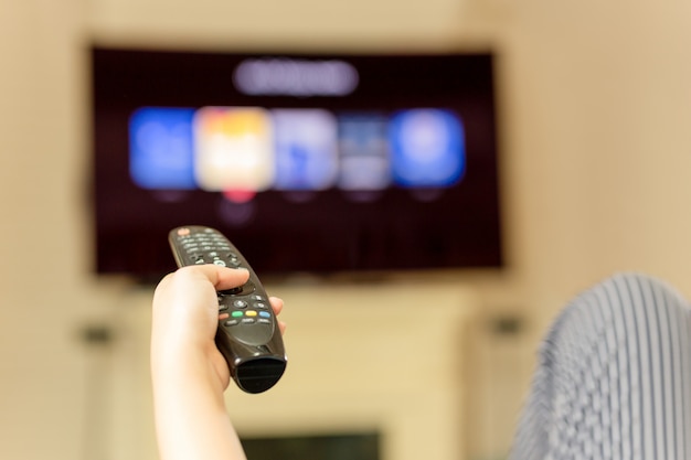 Mão usando o controle remoto para assistir televisão em casa