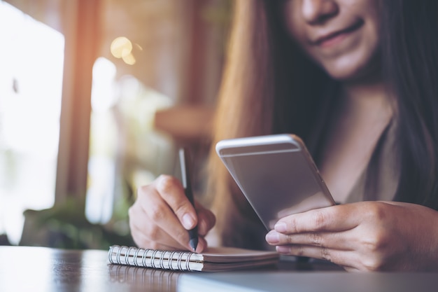 Mão usando telefone e vai anotar no caderno em branco