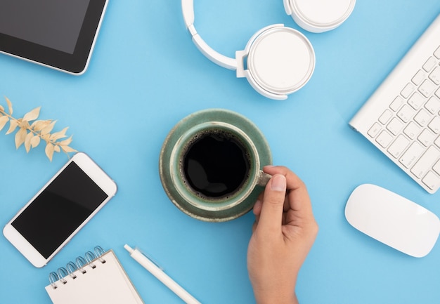 Mão xícara de café, smartphone, fones de ouvido, mouse e teclado e muito mais sobre fundo azul claro