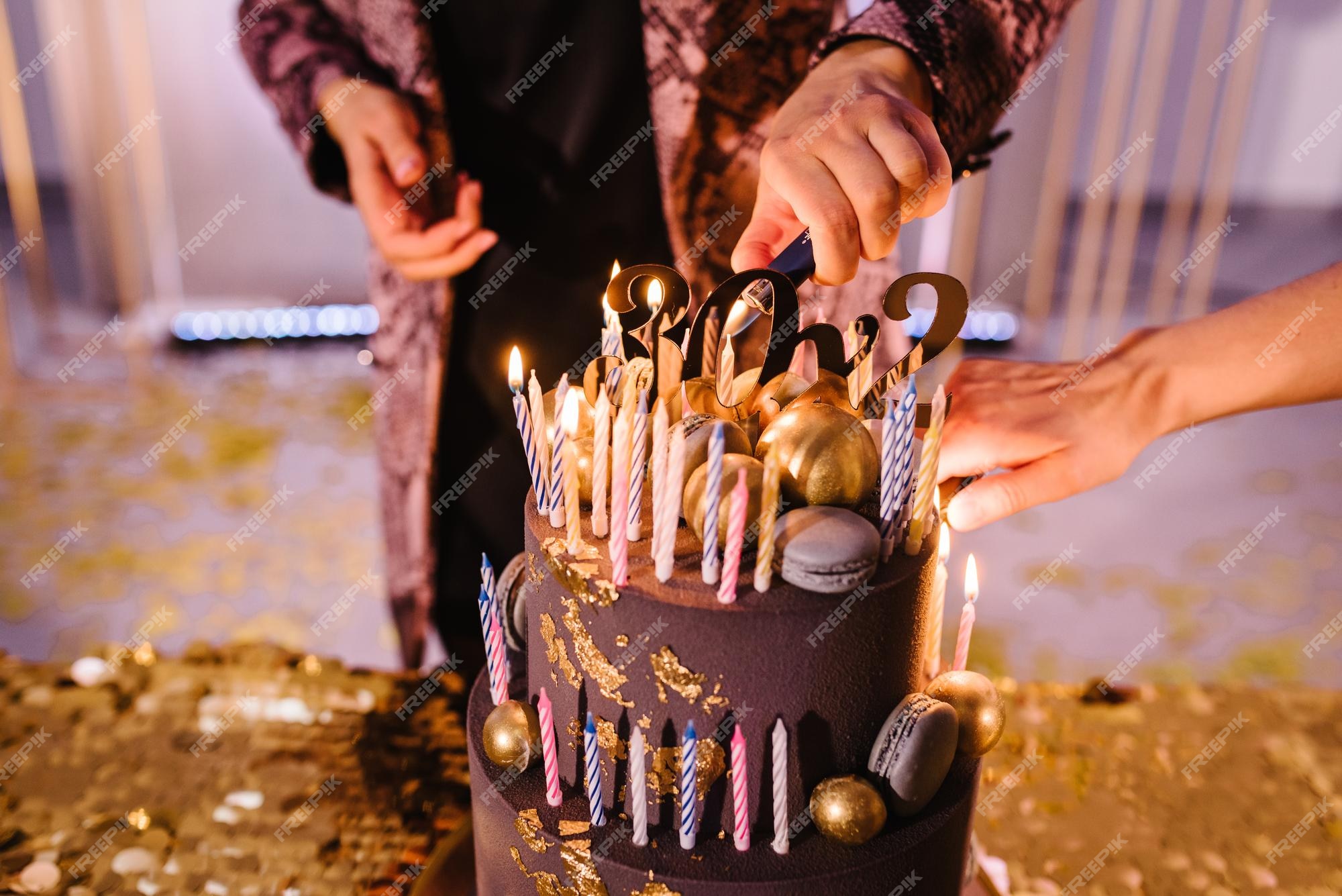 Mãos acendem velas no bolo o bolo de férias é decorado com bolas douradas,  brilhos dourados e macaroons pretos bolo de aniversário masculino 60 anos  fechar