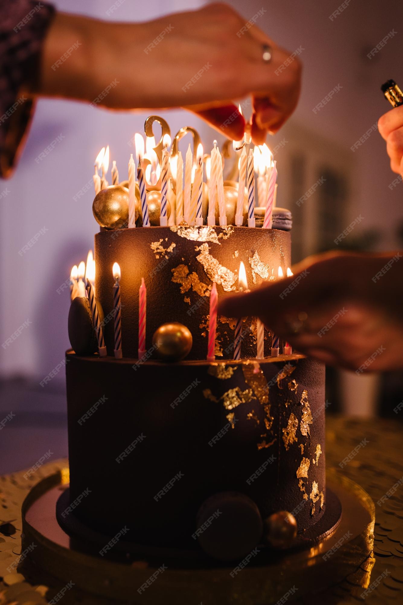 Mãos acendem velas no bolo o bolo de férias é decorado com bolas douradas,  brilhos dourados e macaroons pretos bolo de aniversário masculino 60 anos  fechar