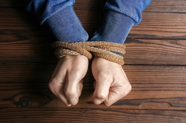 Mãos amarradas com uma corda com risco de vida em um fundo de madeira.