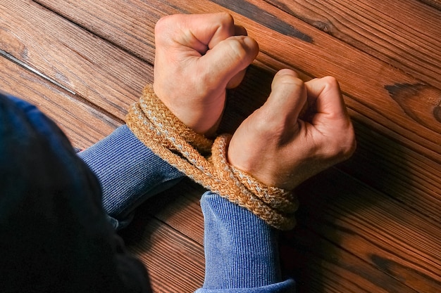 Mãos amarradas com uma corda com risco de vida em um fundo de madeira.