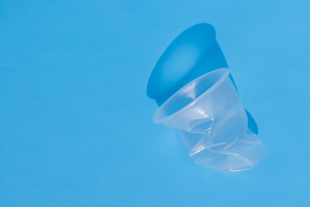 Mãos amassam amassam um copo de plástico em um fundo azul conceito de ecologia sem plástico