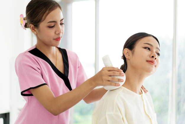 Mãos aproximadas de um massagista segurando massagem de compressa de ervas tailandesa nas costas de uma cliente