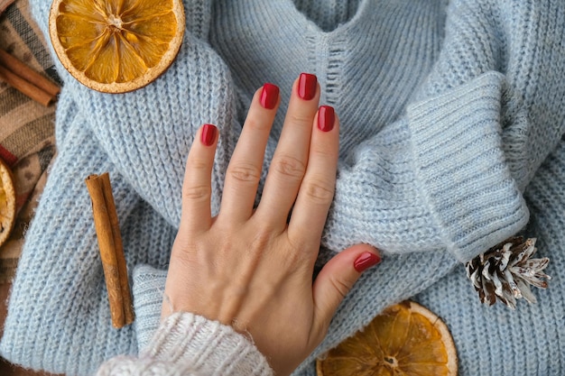 Mãos bem cuidadas de mulher elegantes unhas vermelhas copiam o espaço Camisola azul Closeup Estilo inverno ou outono do conceito de design de unhas Tratamento de beleza