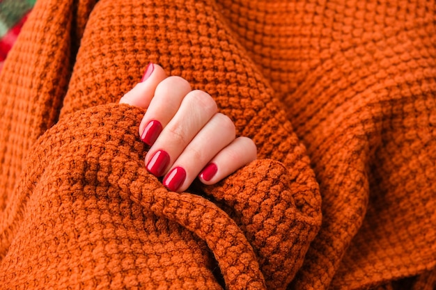 Mãos bem cuidadas de mulher, unhas vermelhas elegantes, copie o espaço Suéter laranja Closeup Estilo de inverno ou outono do conceito de design de unhas Tratamento de beleza