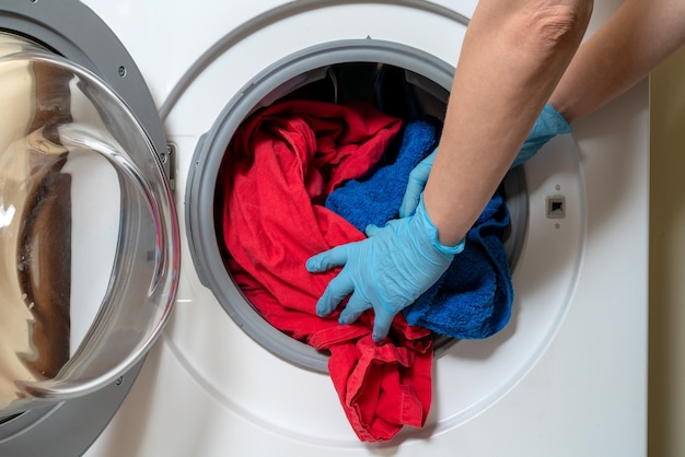 Mãos carregando roupa de cama em uma máquina de lavar