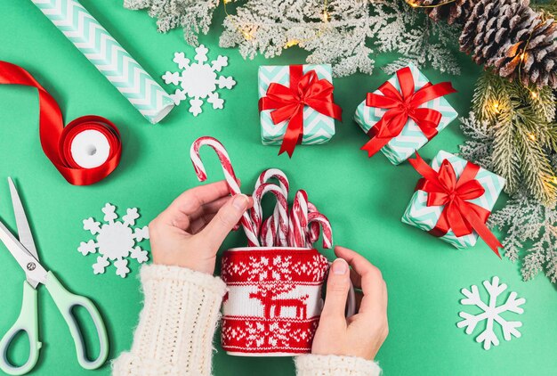 Mãos caucasianas femininas colocam pirulitos em uma caneca em um suéter de natal de malha vermelha