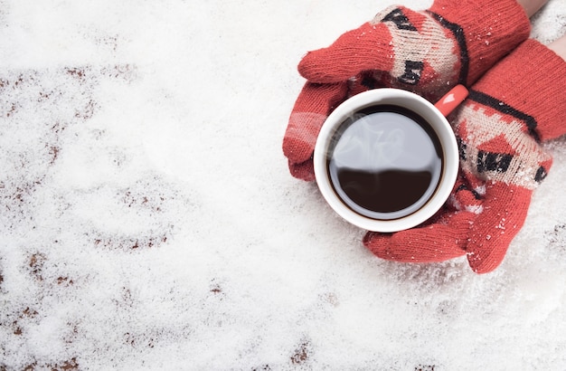 Mãos cobertas segurando caneca de café quente na neve branca