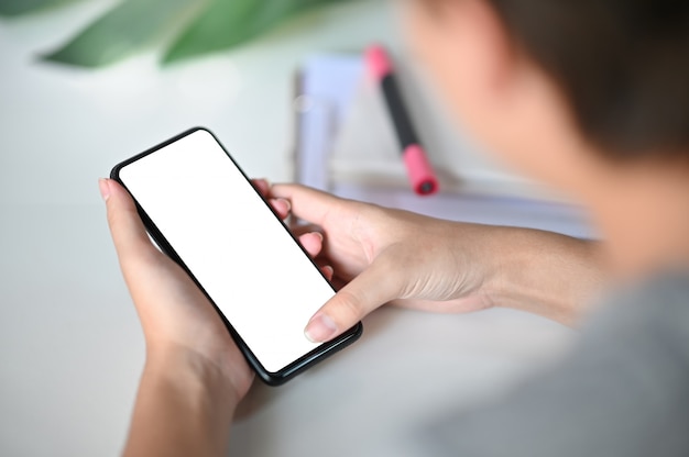 Mãos colhidas do tiro usando o smartphone do modelo na mesa de escritório com trajeto de grampeamento.