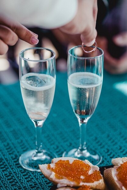 Mãos colocando anéis em taças de casamento com espumante champanhe