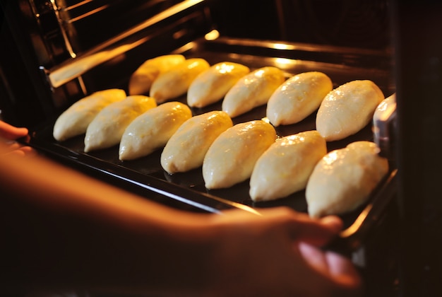 Mãos colocando no forno uma assadeira com tortas de fermento cru