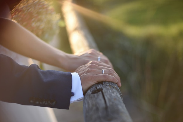 Mãos com anéis de casamento de casal recém-casado ao pôr do sol