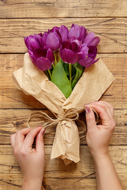 Mãos com buquê de tulipas roxas em papel artesanal na vista superior da mesa de madeira