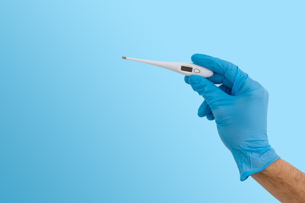 Mãos com luvas azuis segurando um termômetro médico