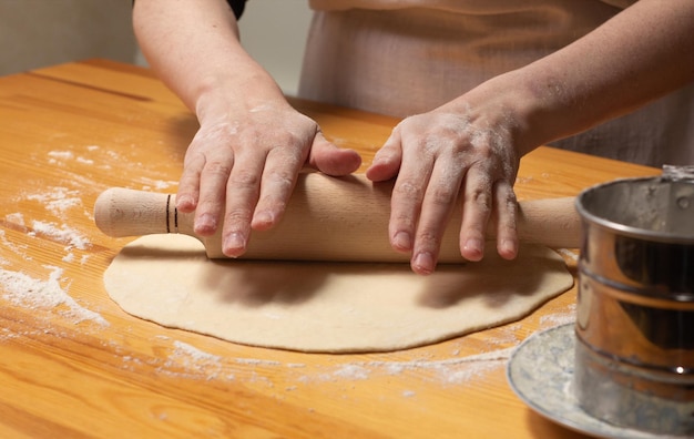 Mãos com rolo fazem massa para pizza Processo de preparação de pizza italiana em mesa de madeira