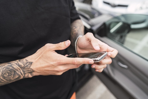 Mãos com tatuagens segurando um telefone perto do carro