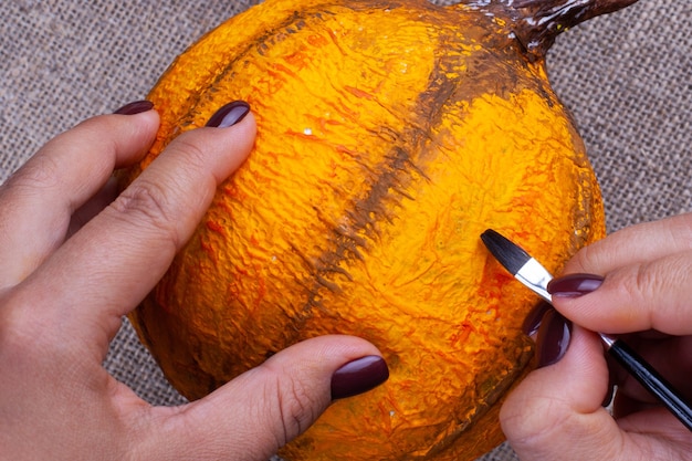 Mãos com tinta de manicure escura com um pincel com guache laranja cores abóbora artesanal de papel machê para o halloween