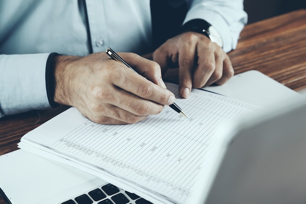 Mãos com um documento e uma caneta em um teclado de computador