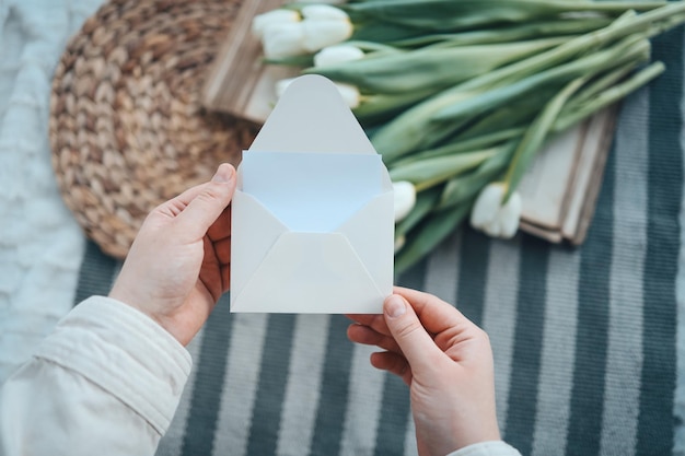 Mãos com um envelope vazio em um fundo de flores, um lugar para o seu texto