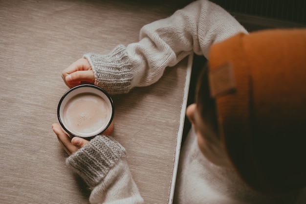 Mãos com um suéter seguram chocolate quente, em uma caneca vermelha, vista superior. uma foto aconchegante com uma caneca na mão com espaço de cópia. criança bebe chocolate quente