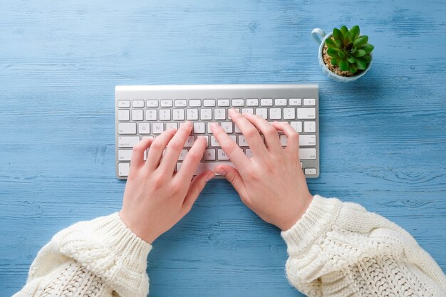 Mãos com um teclado em cima da mesa. garota trabalha no computador.